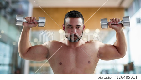 Muscular man lifting dumbbells in gym, focusing on strength training 126485911