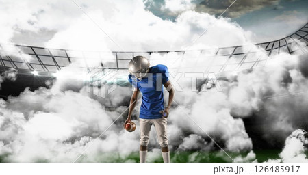 Football player in blue jersey holding ball on field with dramatic clouds Football player in blue jersey holding ball on field with dramatic clouds 126485917