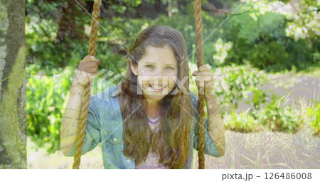 Young girl swinging joyfully on rope swing in sunny garden 126486008