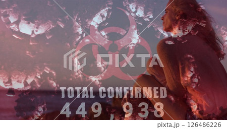 Pensive woman at beach with biohazard symbol and COVID-19 statistics overlay 126486226