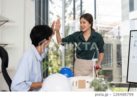 Positive Interaction in Sustainable Design. Colleagues sharing ideas and high-fiving in a modern office. Positive Interaction in Sustainable Design. Colleagues sharing ideas and high-fiving in a modern office. 126486799