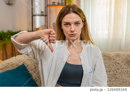 Adult sad woman showing thumbs down at home, looking serious, expressing disagreement disapproval Adult sad woman showing thumbs down at home, looking serious, expressing disagreement disapproval 126489169
