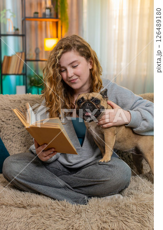 Young woman reading bedtime story to pug dog on home sofa, peaceful end of day with emotional care 126489180