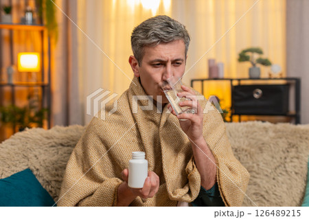 Young man takes pill with tired expression while holding head in pain from headache or migraine Young man takes pill with tired expression while holding head in pain from headache or migraine 126489215