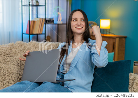 Young woman happily closing laptop on sofa celebrating successful project smiling victory sign Young woman happily closing laptop on sofa celebrating successful project smiling victory sign 126489233