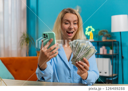 Happy rich businesswoman counting money dollar cash using smartphone calculator app at home office 126489288