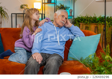 Loving worried kind girl granddaughter consoling sad crying grandfather helping with problem at home Loving worried kind girl granddaughter consoling sad crying grandfather helping with problem at home 126489296