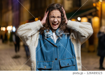 Displeased angry girl frowns face feels disgust suffering from loud sound covers ears with hands Displeased angry girl frowns face feels disgust suffering from loud sound covers ears with hands 126489323