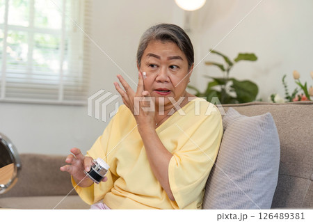 Beauty and Age Diversity. A senior woman applying eye cream, focusing on her skincare routine. 126489381