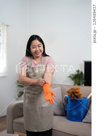 Preparation for Cleaning. A woman putting on orange gloves in her living room. Preparation for Cleaning. A woman putting on orange gloves in her living room. 126489437