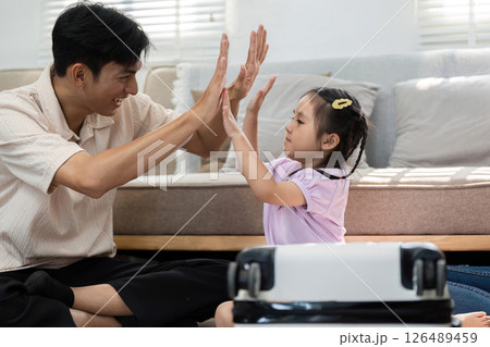 Playful Interaction and Family Engagement. A father and daughter sharing a playful moment with a suitcase. 126489459