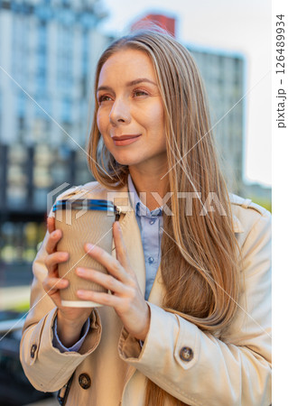 Happy mature businesswoman enjoying morning coffee hot drink and smiling on downtown city street 126489934