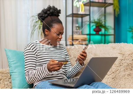 African American young woman surprised using credit card, checking laptop screen worried about fraud African American young woman surprised using credit card, checking laptop screen worried about fraud 126489969
