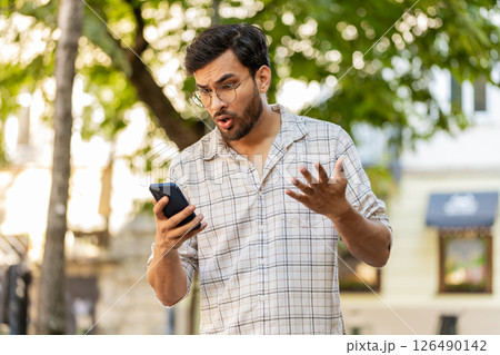 Indian young man using smartphone loses becoming surprised sudden lottery results standing on street 126490142