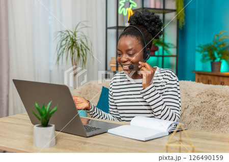 African American woman working call center operator headset on sofa, focused writing notes, home 126490159