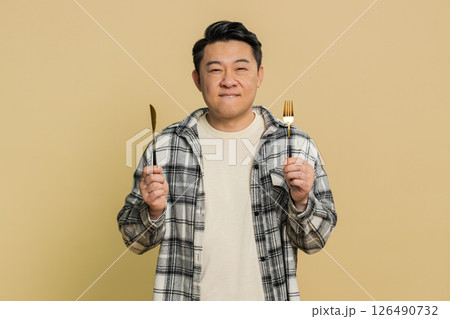 Hungry Asian man waiting for serving dinner meal dishes with restlessness holding cutlery fork knife 126490732