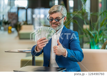 Rich mature businessman putting on thug life sunglasses showing money dollar in modern office lobby 126490760