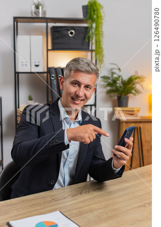 Smiling Caucasian businessman pointing at smartphone, pointing on mobile screen app at home office 126490780