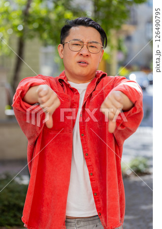 Upset Asian man showing thumbs down sign, disapproval, dissatisfied bad work, mistake in city Upset Asian man showing thumbs down sign, disapproval, dissatisfied bad work, mistake in city 126490795