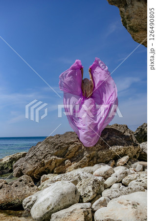 Plastic pollution ocean: Purple bag flies on rocky beach, littering the sea on a sunny day due to wind. 126490805