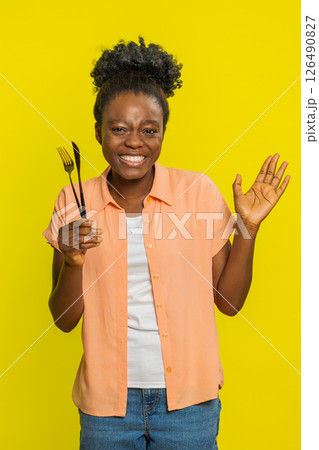 African American woman holding fork and knife, inviting gesture, friendly smile, shared meal food 126490827