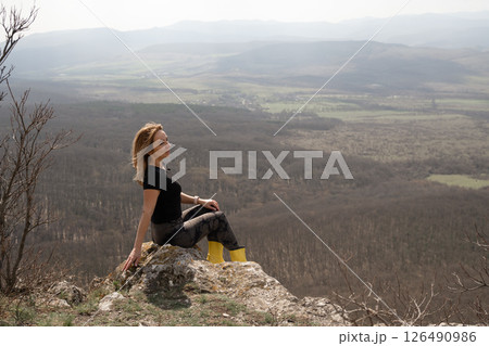 Woman Landscape Relaxation: Lady rests on rock outcrop above scenic valley landscape, sunny day for enjoying view. Woman Landscape Relaxation: Lady rests on rock outcrop above scenic valley landscape, sunny day for enjoying view. 126490986