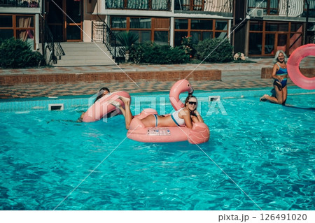 A woman is floating in a pink flamingo float in a pool. The pool is surrounded by a brick wall and has a few other people in the background. 126491020