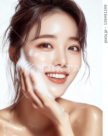 Smiling woman applying cleansing foamy product on her face during a skincare routine in a bright studio setting 126491209