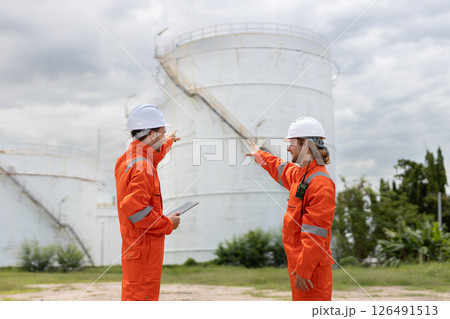 Worker in safety gear using tablet near industrial storage oil tanks refining petrochemical industry factory. 126491513