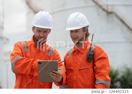 Worker in safety gear using tablet near industrial storage oil tanks refining petrochemical industry factory. 126491525