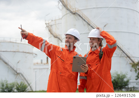 Worker in safety gear using tablet near industrial storage oil tanks refining petrochemical industry factory. 126491526