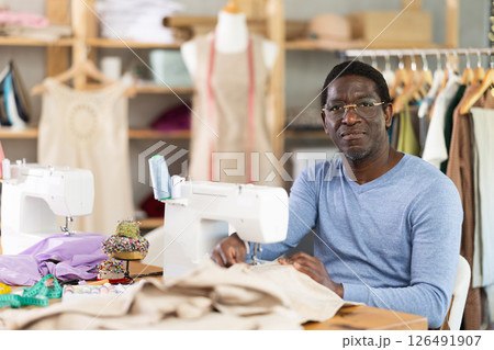 African American man tailor sews clothes in sewing machine. African American man tailor sews clothes in sewing machine. 126491907
