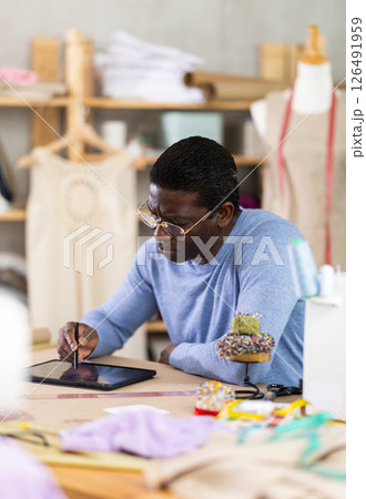 Male dressmaker working on digital sketch of dress in workshop 126491959