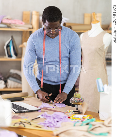Male tailor cutting fabric with scissors while working in workshop Male tailor cutting fabric with scissors while working in workshop 126491978
