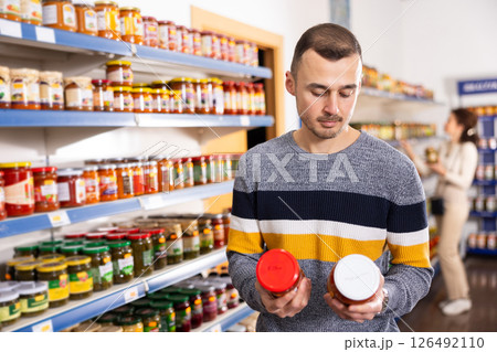 Man shopper wants to buy jar of delicious lecho in grocery store Man shopper wants to buy jar of delicious lecho in grocery store 126492110