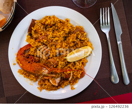 Paella made of rice and different seafood served in plate with table appointments Paella made of rice and different seafood served in plate with table appointments 126492236