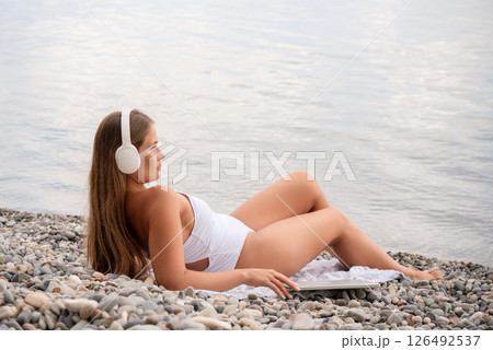 A woman is laying on the beach with a laptop and headphones on 126492537