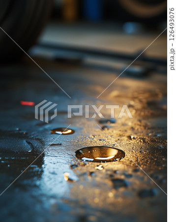 Motor oil change process captured from floor level with spilled oil on the ground in a garage 126493076