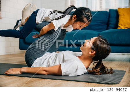 In a harmonious family fitness session a mother and her child playfully pretend to 'fly' like airplanes while practicing Pilates and yoga enhancing their bond trust and happiness. 126494077