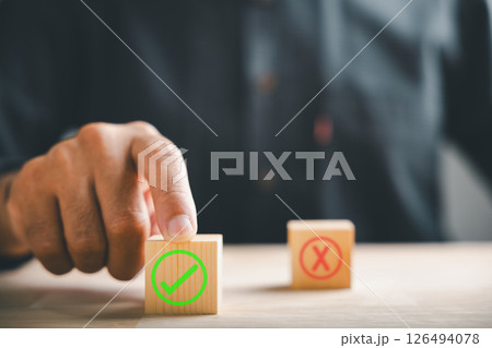Finger of businessman touches wooden cubes with check marks showing right and wrong choices. Communicates choice validation in decision-making. Think With Yes Or No Choice. Finger of businessman touches wooden cubes with check marks showing right and wrong choices. Communicates choice validation in decision-making. Think With Yes Or No Choice. 126494078
