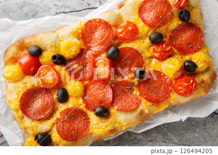 Italian pinsa romana with tomato mix, peperoni sausage, olive and cheddar cheese closeup on parchment. Horizontal top view 126494205