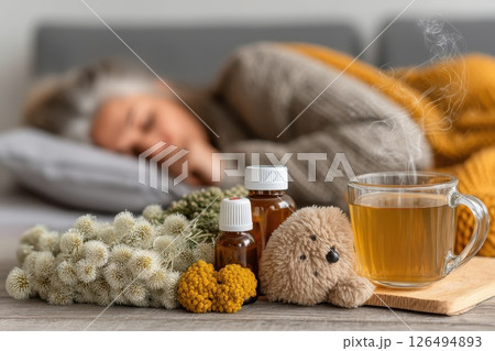 Woman Lying in Bed Looking Pale and Uncomfortable with Herbal Remedies and Cup of Tea 126494893