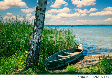 View of the lake in summer on a sunny day. Wooden boat on the lakeshore View of the lake in summer on a sunny day. Wooden boat on the lakeshore 126497135