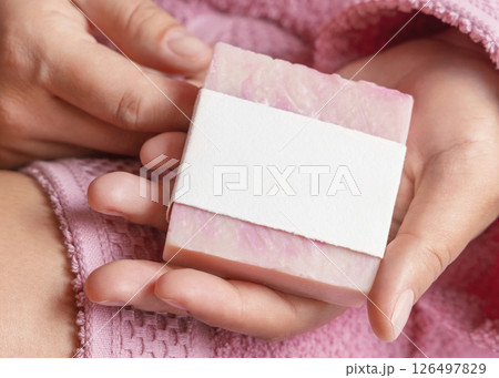 Closeup of woman in pink bathrobe holding soap bar with blank label in hands, mockup 126497829