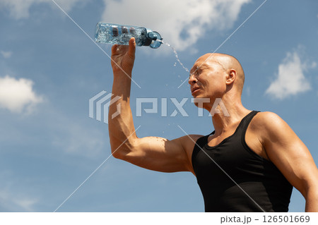 Sweaty handsome sporty man refreshing himself water from bottle against blue sky at summer heat after training outdoors. Concept water balance. Close up. Banner. Sweaty handsome sporty man refreshing himself water from bottle against blue sky at summer heat after training outdoors. Concept water balance. Close up. Banner. 126501669