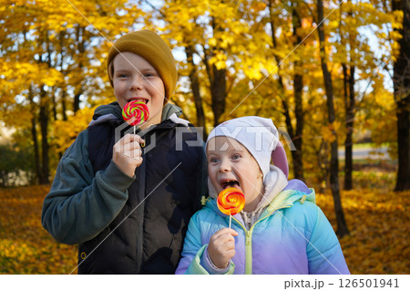 Portrait of a boy and a girl eating lollipops in an autumn park. Portrait of a boy and a girl eating lollipops in an autumn park. 126501941