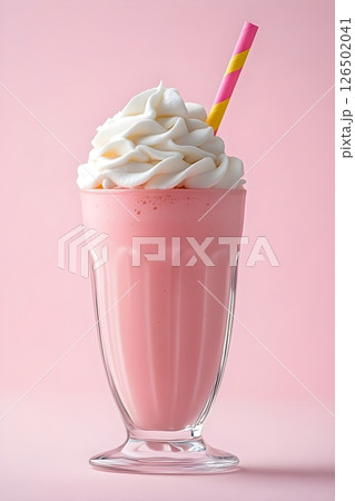 Strawberry milkshake in a classic tall glass against a pink background. The beverage features a generous swirl of white whipped cream on top and is served with a pink and yellow striped paper straw. Strawberry milkshake in a classic tall glass against a pink background. The beverage features a generous swirl of white whipped cream on top and is served with a pink and yellow striped paper straw. 126502041