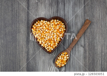Unpopped popcorn in a wooden bowl on wooden background. A type of corn that expands from the kernel and puffs up when heated. Yellow seeds, edible, raw and vegan food. Isolated macro photo close up. Unpopped popcorn in a wooden bowl on wooden background. A type of corn that expands from the kernel and puffs up when heated. Yellow seeds, edible, raw and vegan food. Isolated macro photo close up. 126503051
