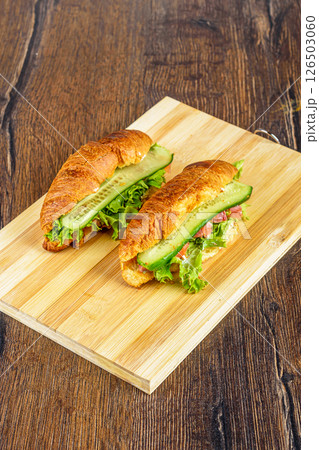 Cutting board with croissants stuffed with lettuce leaves and soft cheese, pieces of red fish and cucumbers. Cutting board with croissants stuffed with lettuce leaves and soft cheese, pieces of red fish and cucumbers. 126503060