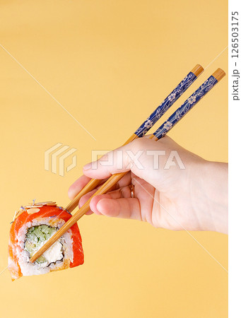 Hand Holding Salmon Sushi Roll with Chopsticks on Yellow Background Hand Holding Salmon Sushi Roll with Chopsticks on Yellow Background 126503175